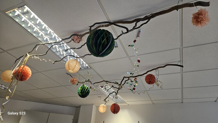 An einer Decke aus Spanplatten hängen zwei Äste, an denen verschiedenen Dekogegenstände angebracht sind.