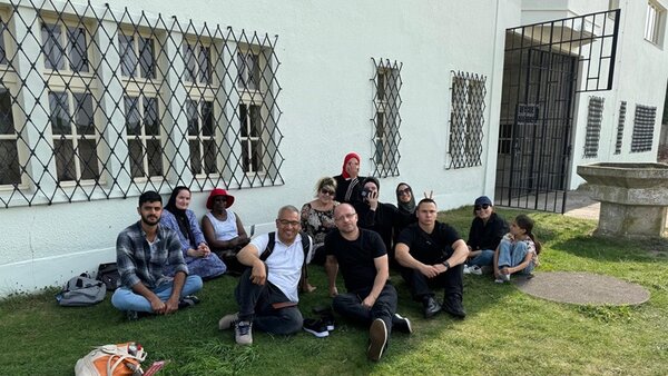 Die Teilnehmenden und ihr Lehrer posieren sitzend vor der Gedänkstätte Sachsenhausen für ein Gruppenfoto.