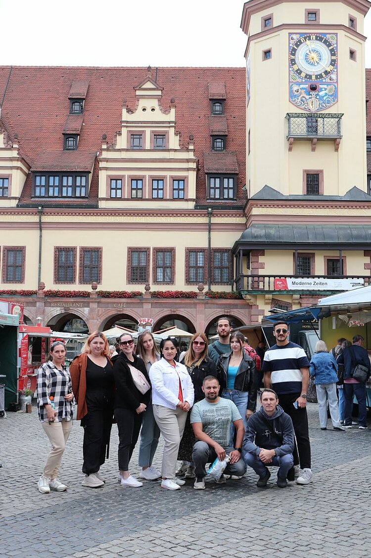 Unser Integrationskurs besucht Leipzig Gruppenfoto von elf Personen auf einem Platz vor dem Alten Rathaus in Leipzig, im Hintergrund die Fassade mit Turmuhr.