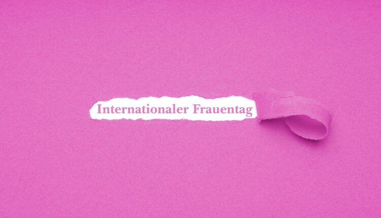 Ein pinkes Blatt Papier, aus dem ein Streifen gerissen ist: dort steht "Internationaler Frauentag".