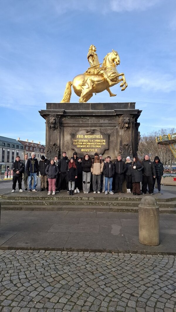 Gruppenfoto vor dem Goldenen Reiter in Dresden: Menschen stehen auf den Stufen des Denkmals, über ihnen die vergoldete Reiterstatue auf hohem Sockel