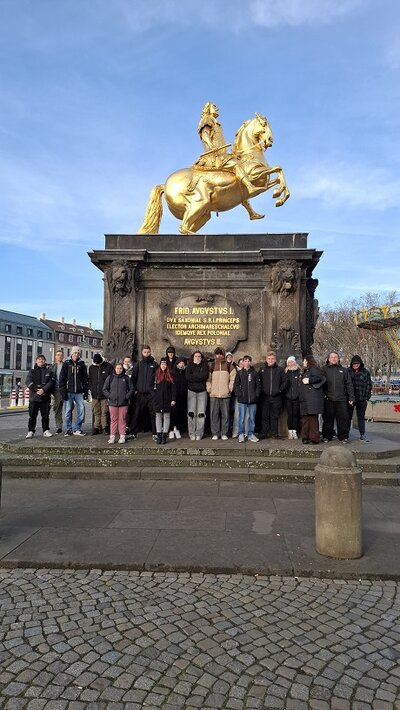 Gruppenfoto vor dem Goldenen Reiter in Dresden: Menschen stehen auf den Stufen des Denkmals, über ihnen die vergoldete Reiterstatue auf hohem Sockel