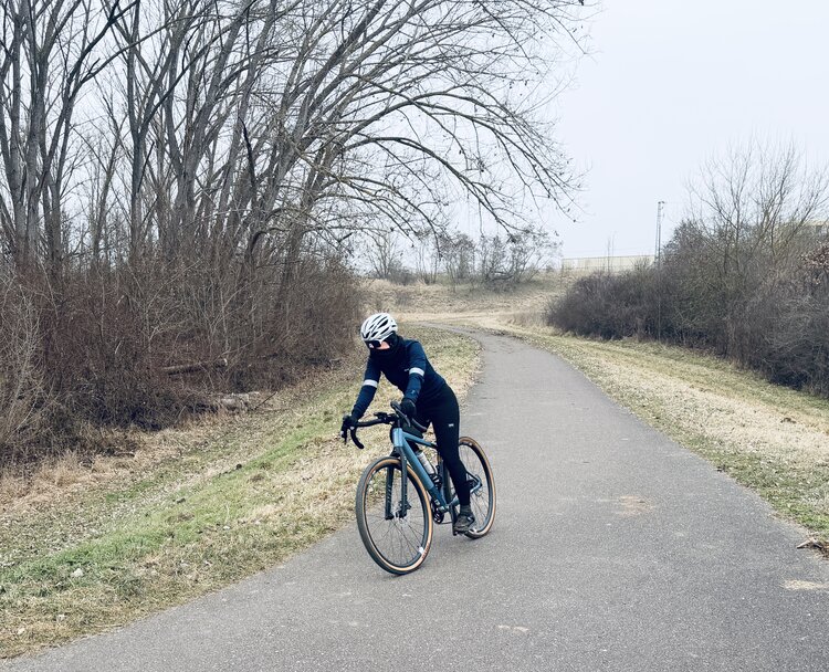 Auf einem mit Laub bedeckten Radweg fährt ein Radfahrer mit Helm und schwarzer Kleidung.
