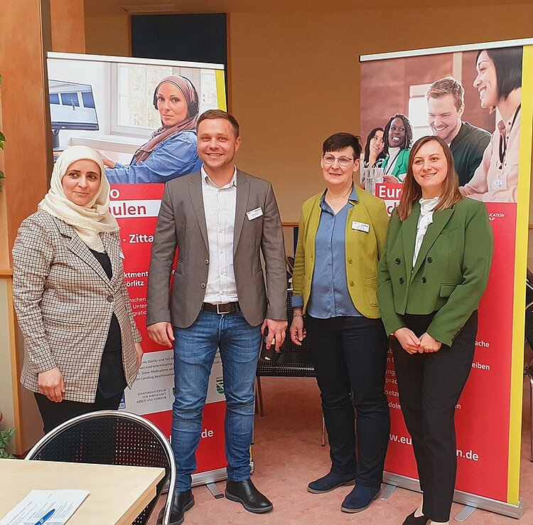 Gelungene Auftaktberatung der Arbeitsmarktmentoren Vier Teilnehmende stehen vor großen Euro-Schulen Roll-Ups im Hintergrund und posieren gemeinsam für ein Gruppenfoto.