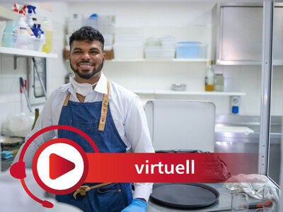 Ein lächelnder Mann in einer Küchenumgebung trägt eine blaue Schürze über einem weißen Hemd und Handschuhe. Er steht vor einem Arbeitstisch, auf dem eine Pfanne und andere Küchenutensilien zu sehen sind. Im Vordergrund ist ein rotes Symbol mit einem Play-Button und dem Wort 'virtuell' eingeblendet. Im Hintergrund sind Regale mit Küchenzubehör wie Reinigungsmitteln und Behältern zu erkennen.