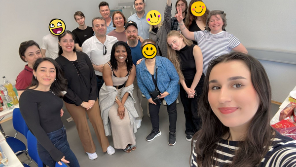 Gruppen-Selfie eines B2-Kurses in einem Klassenraum; mehrere Teilnehmende stehen eng zusammen und lächeln in die Kamera, einige Gesichter sind mit Smileys verdeckt.