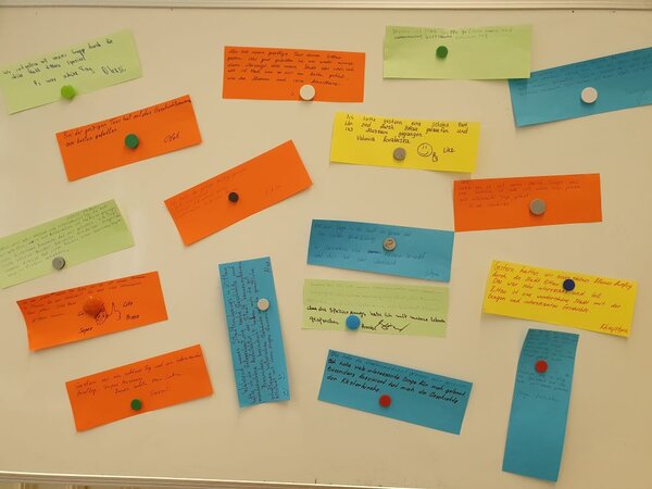 Eine Pinnwand mit mehreren bunten Feedback-Karten, auf denen handschriftliche Kommentare und Meinungen zu sehen sind. Die Karten sind in verschiedenen Farben gehalten und mit Magneten oder Pinnnadeln befestigt.