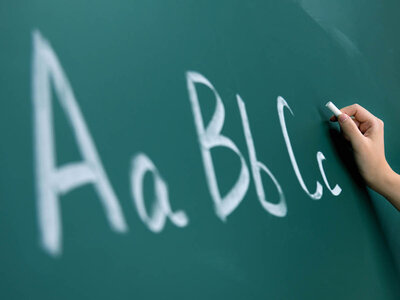 Eine Hand schreibt mit weißer Kreide die Buchstaben 'Aa, Bb, Cc' auf eine grüne Tafel. Die Buchstaben sind in Groß- und Kleinbuchstaben geschrieben und dienen wahrscheinlich als Beispiel für die Schreibweise von Buchstaben.