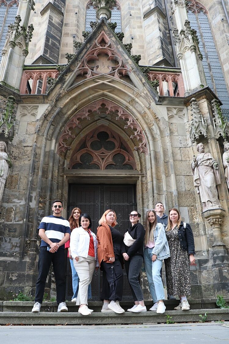 Unser Integrationskurs besucht Leipzig Acht Personen stehen vor dem Eingang einer alten Kirche mit reich verzierten gotischen Steinfiguren.
