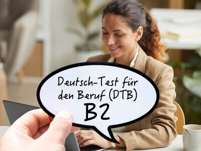 Eine Frau mit einem beigen Blazer sitzt an einem Tisch und lächelt, während sie auf einen Laptop schaut. Vor ihr schwebt eine Sprechblase mit dem Text 'Deutsch-Test für den Beruf (DTB) B2'. Der Hintergrund ist unscharf und zeigt einen modernen Arbeitsplatz."