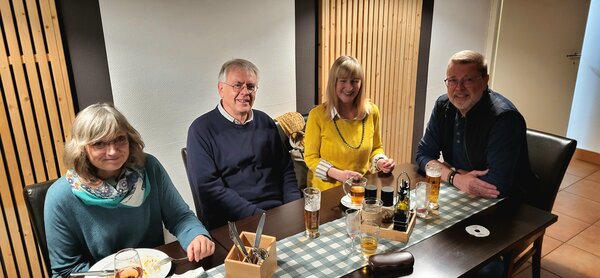 Zwei männliche und zwei weibliche Mitarbeiter*innen der Euro-Schulen bzw. Euro Akademie, die zusammen an einem Tisch in einem Restaurant sitzen und etwas essen und in die Kamera lächeln.