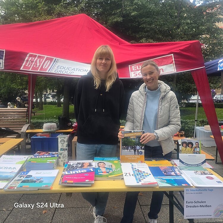 Zwei gut gelaunte Mitarbeiterinnen stehen am Stand der Euro-Schulen und lächeln in die Kamera. 