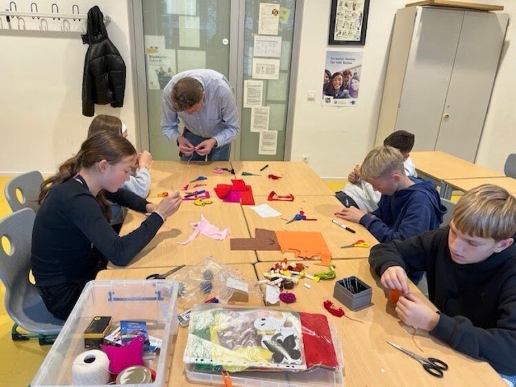 Schülerinnen und Schüler der 7. Klasse der Sportoberschule Leipzig arbeiten konzentriert in einem Klassenraum an kreativen Aufgaben mit Stoff- und Bastelmaterialien im Rahmen der Potenzialanalyse ‚Profil AC Sachsen‘ der Euro-Schulen Leipzig. Auf den Tischen liegen farbige Materialien, Werkzeuge und Bastelutensilien, während die Jugendlichen gemeinsam praktische Aufgaben bearbeiten.