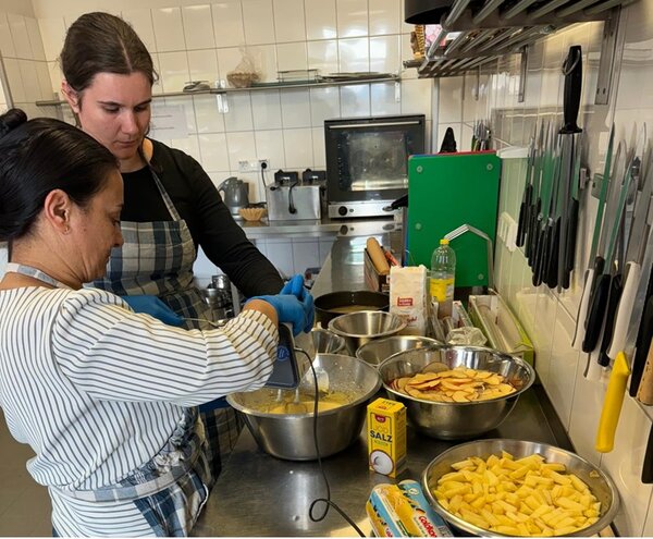 Zwei Teilnehmerinnen stehen in der Küche und bereiten gemeinsam Apfelkuchen aus den selbst geernteten Äpfeln zu.