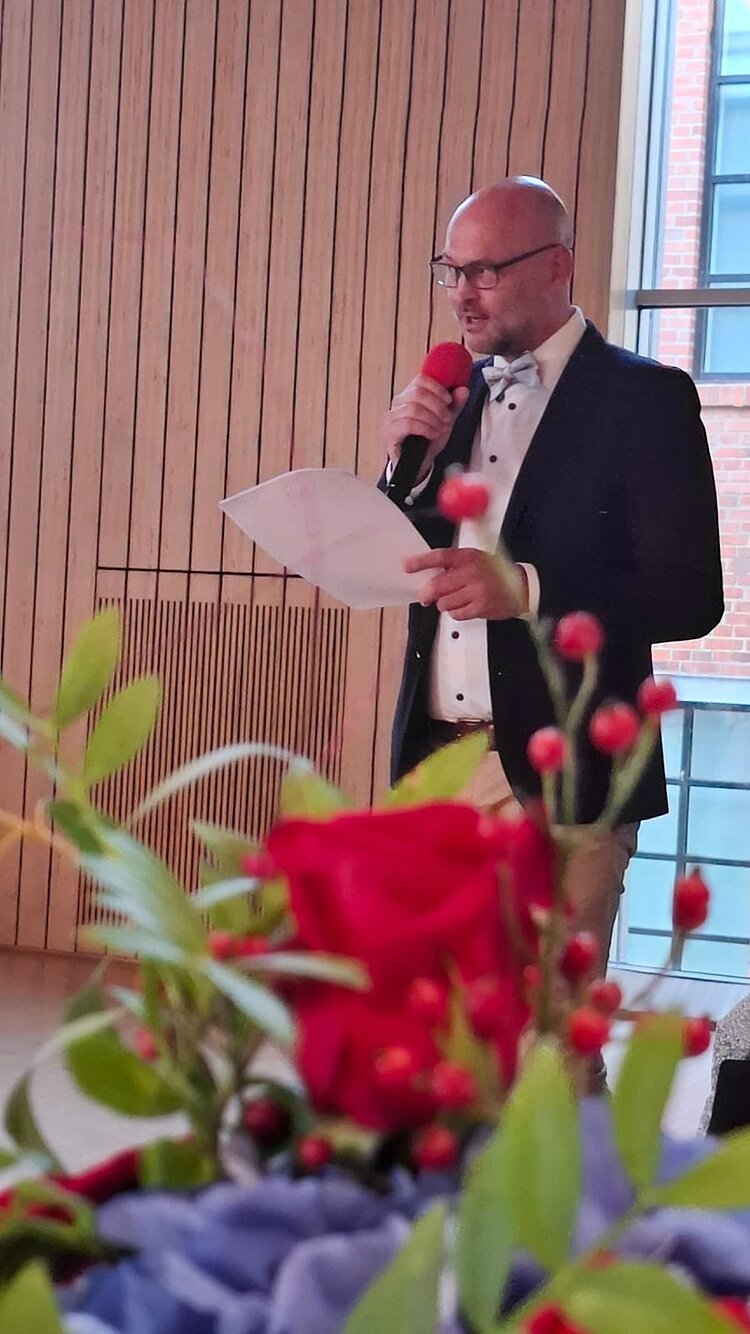 Drei Jahrzehnte voller Wissen und Engagement Leiter der Euro Akademie und der Euro-Schulen Zwickau Herr Hausmann hält eine Rede, er spricht ins Mikrofon und liest von einem Zettel ab.