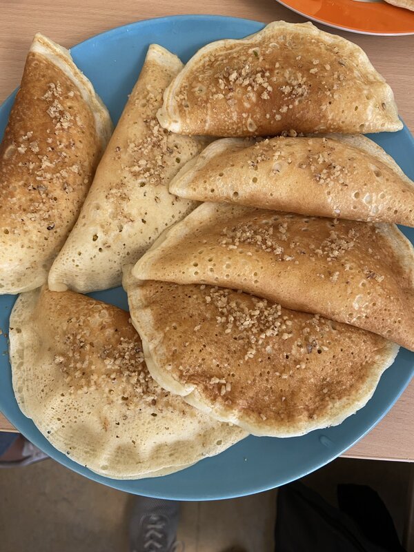 Ein blauer Teller mit mehreren goldbraun gebackenen Atayef, die mit Nüssen bestreut sind. Die gefüllten Teigtaschen sind halbmondförmig zusammengeklappt.