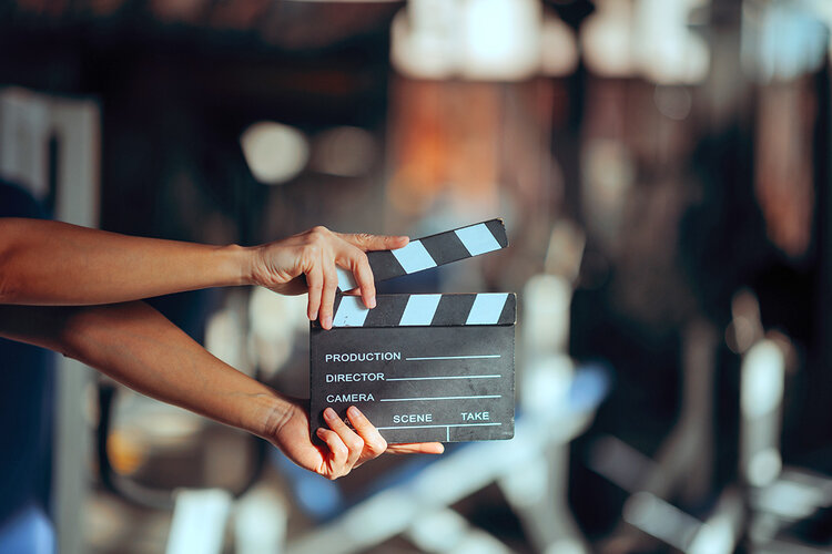 Eine Filmklappe wird vor einem unscharfen Hintergrund gehalten und symbolisiert den Start einer Video- oder Filmproduktion.