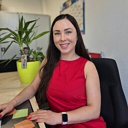 Frau Cozacenco Portrait von Frau Cozacenco am Schreibtisch in einem roten Kleid mit rot lackierten Fingernägel und langen schwarzen Haaren.