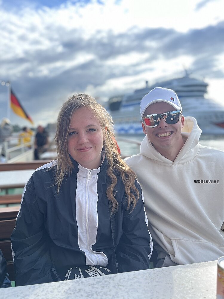 Abschlussfahrt der VK21 an die Ostsee Eine Schülerin und ein Schüler grinsen auf einem Boot in die Kamera.