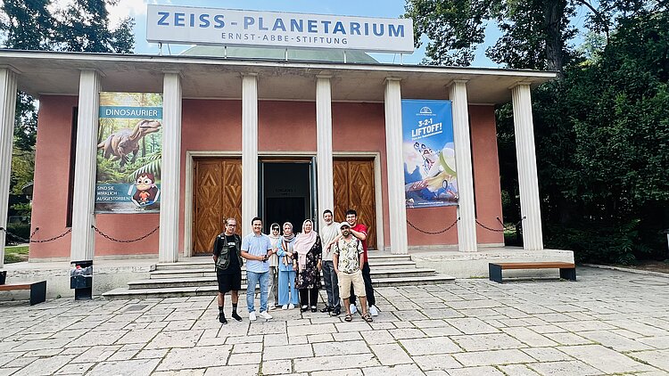 Besuch des Planetariums in Jena und des Landtags in Erfurt Schülerinnen und Schüler der Euro-Schulen Erfurt stehen vor dem Planetarium für ein Gruppenfoto. Das Planetarium hat am Eingang sieben römische Säulen und die Fassade ist hautfarben gestrichen.
