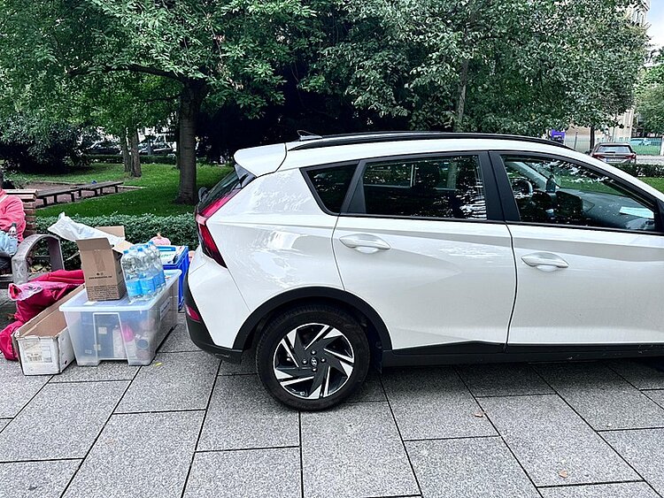 Alle Infomaterialien, der noch unaufgebaute Messestand usw. liegen ausgepackt am Boden neben dem weißen Auto.