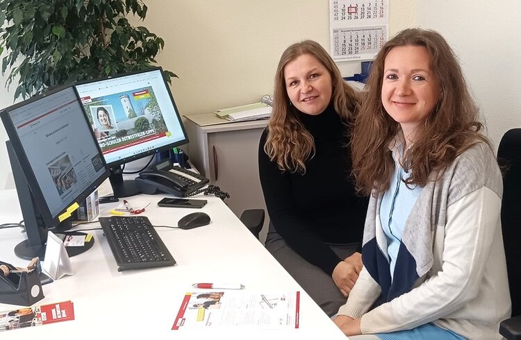 Zwei Mitarbeiterinnen der Euro-Schulen Hoyerswerda, die zusammen die Teilnehmenden der Maßnahme Integration PLUS betreuen, sitzen gemeinsam an einem Arbeitsplatz im Büro. Auf dem Schreibtisch stehen Computer mit der Website der Euro-Schulen, Telefon und Informationsmaterialien. Das Foto zeigt eine freundliche Büroszene, die für Beratung, Weiterbildung und Teamarbeit bei den Euro-Schulen Hoyerswerda steht. Beide Mitarbeiterinnen lächeln in die Kamera, während sie für das Foto posieren.