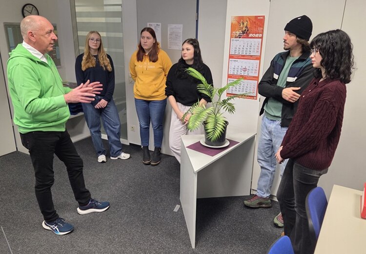 Herr Köhler vom Hospiz berichtet interessierten Auszubildenden und Teilnehmenden, die gemeinsam mit ihm im Raum stehen, von der Arbeit im Hospiz.