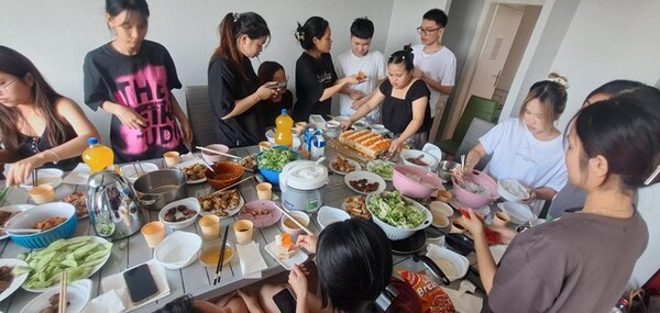 Letzte Vorbereitungen der Teilnehmenden, die ihre Gerichte auf der langen eingedeckten Tafel platzieren.