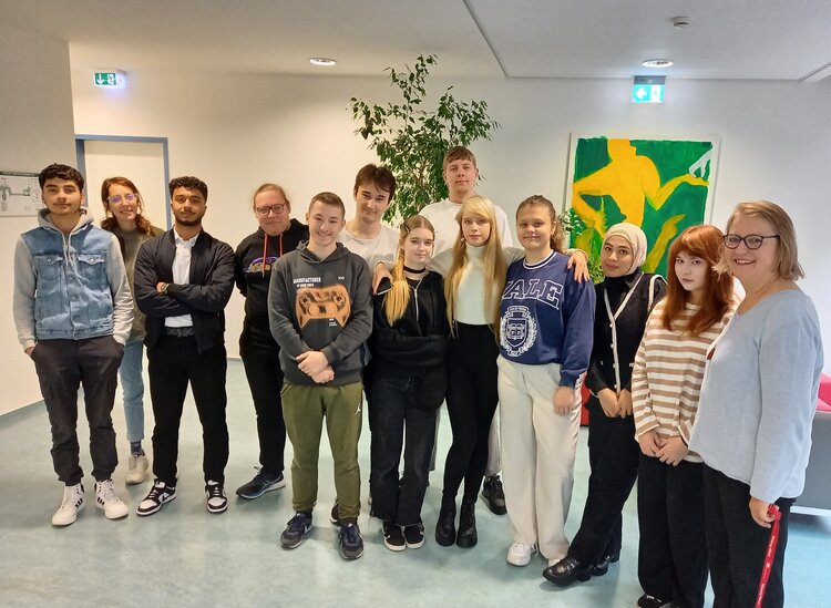 Junge Menschen beider Geschlechter stehen in einem Flur und lächeln in die Kamera.