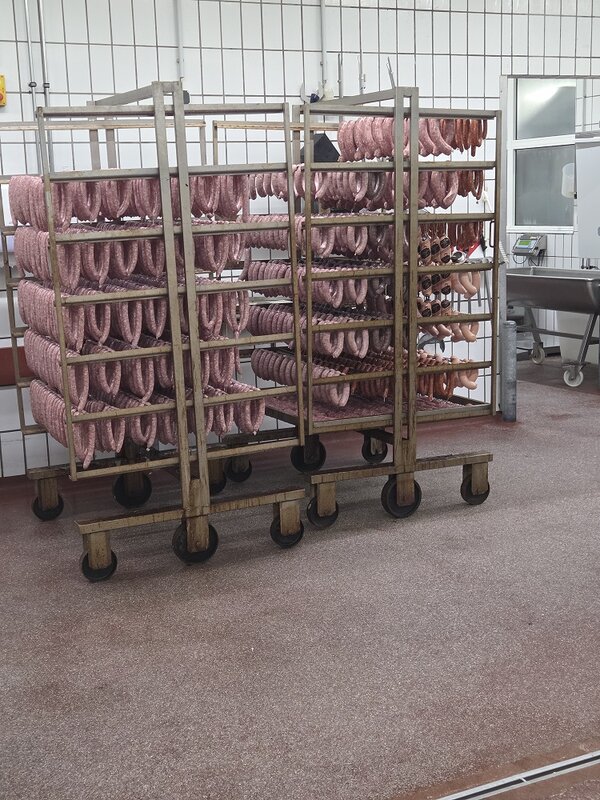 Mehrere fahrbare Edelstahlwagen mit zahlreichen aufgehängten Würsten in einer Lebensmittelproduktionshalle.