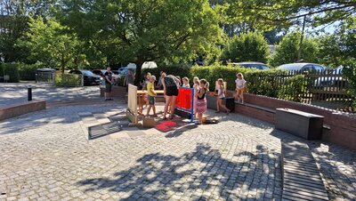 Auf dem Bild sind Kinder auf einer gepflasterten Fläche zu sehen, die Spielzeug aufbauen.