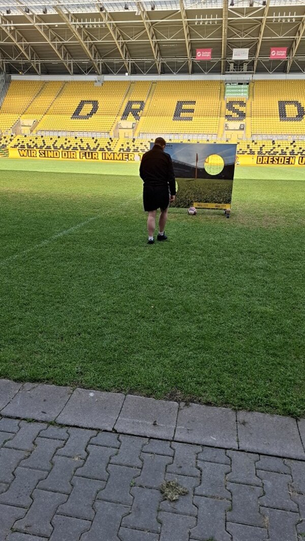 Ein Teilnehmer steht auf dem Stadionrasen vor einer Torwand, bereit zum Schuss mit dem Fußball – sportlicher Spaß im Profiumfeld.