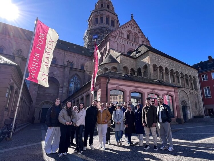 Die Teilnehmenden des Orientierungskurses posieren bei strahlendem Sonnenschein auf dem Mainzer Marktplatz für ein Gruppenbild.
