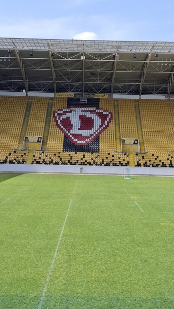 Nahaufnahme der Tribüne mit dem großflächig gestalteten Vereinslogo von SG Dynamo Dresden, eingebettet in die gelbe Sitzlandschaft.