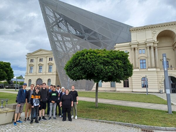 Die Teilnehmenden stehen vor dem beeindruckenden Gebäude des Militärhistorischen Museums in Dresden, das in der architektonischen Stilrichtung des Dekonstruktivismus gebaut wurde.