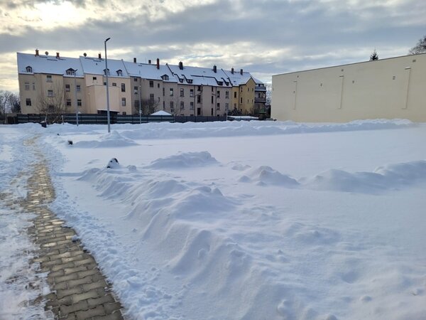 Blick auf einen verschneiten Platz, im Hintergrund ein großes Gebäude.