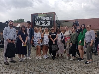 Die heterogene Gruppe der Teilnehmenden des B2-Berufssprachkurses an den Euro-Schulen Potsdam posieren gemeinsam und gut gelaunt vor der JOBinale-Messe für ein Gruppenfoto.