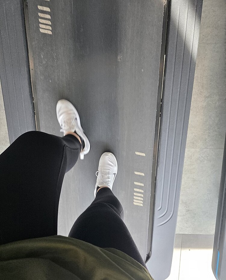 Unsere Teams laufen los – REWE Team Challenge 2025 Ein Laufband von oben fotografiert, zeigt zwei Beine einer Mitarbeitenden in dunkler Sportleggings, mit weißen Turnschuhen, die für den Lauf trainiert.