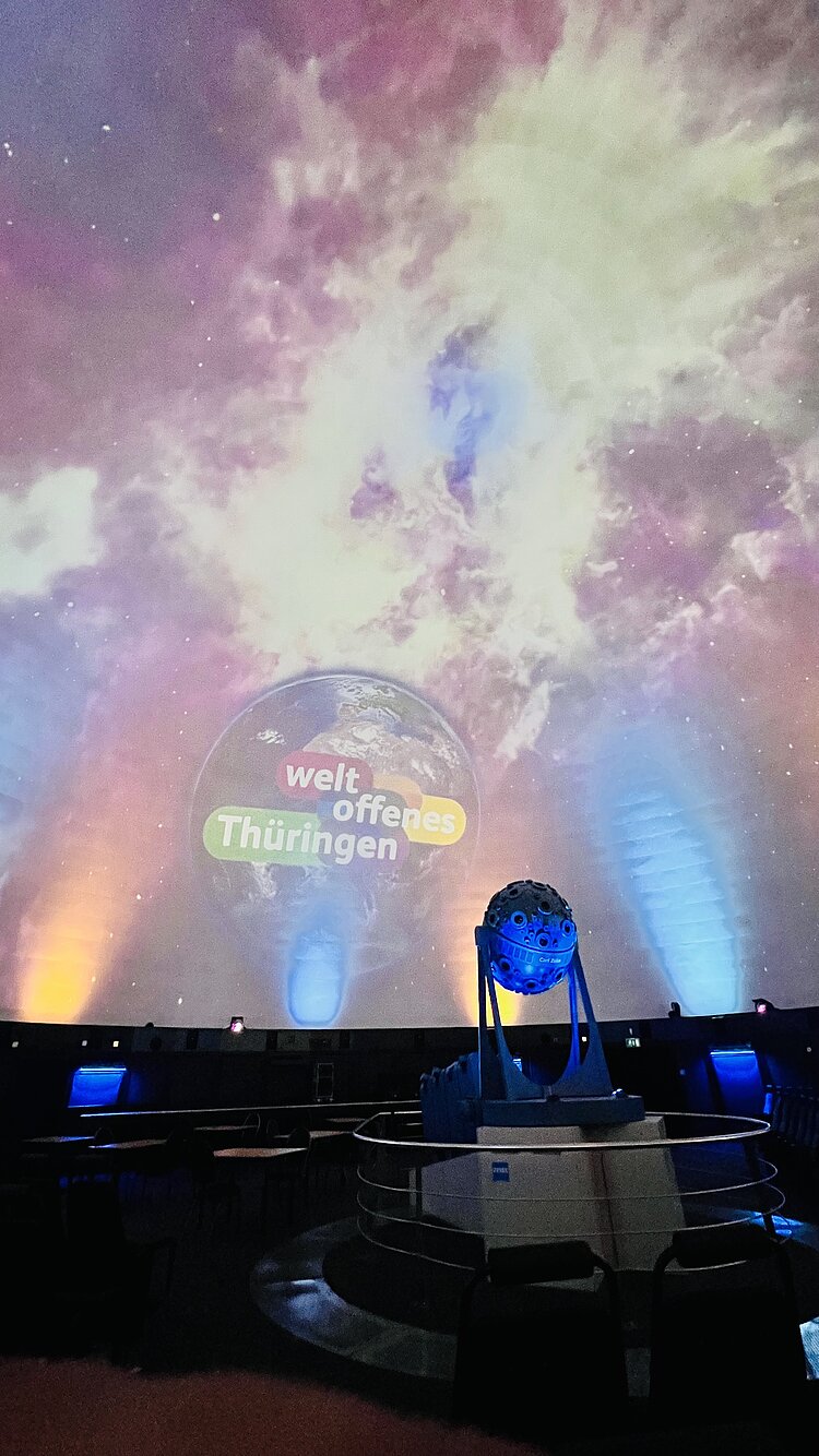 Besuch des Planetariums in Jena und des Landtags in Erfurt Das Bild zeigt die Decke in einem Planetarium, welche mit Holoprojektoren bestrahlt werden und einen Nebel im Weltraum zeigen, der bunt leuchtet.wird und einen großen