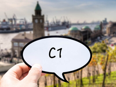 Eine Hand hält eine Sprechblase mit der Aufschrift 'C1' in den Vordergrund. Im Hintergrund ist der Hamburger Hafen mit einem markanten Uhrturm und verschiedenen Gebäuden zu sehen. Der Hafen ist mit Kränen und Schiffen ausgestattet, und der Himmel ist leicht bewölkt.