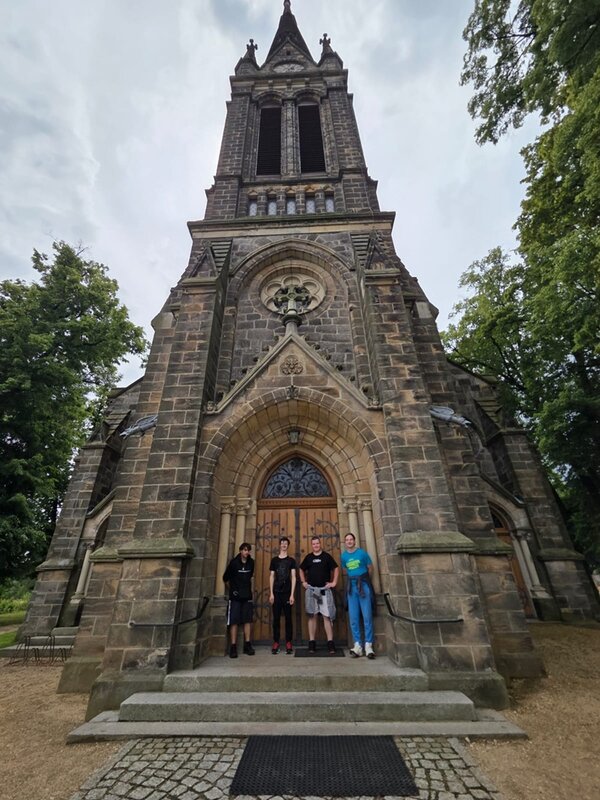 Die Auszubildenden posieren auf den Stufen einer architektonisch im gothischen Stile errichteten Kirche für ein Bild. 