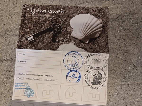 Geöffneter Pilgerausweis für den Ökumenischen Pilgerweg durch Sachsen, Sachsen-Anhalt und Thüringen mit mehreren gesammelten Stempeln.