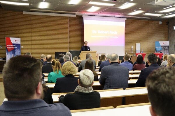 Viele Personen sitzen im Vorlesungsraum einer Hochschule und hören einem Redner ganz vorne zu.