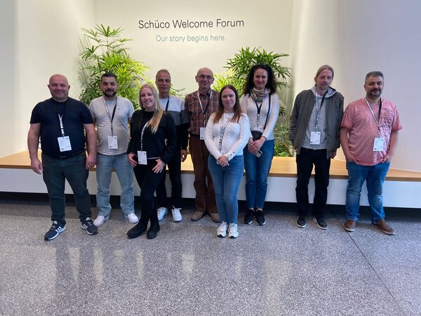 Gruppenbild in einem Foyer mit hellem Licht und Pflanzen; die Teilnehmenden tragen alle einen Besucherausweis um den Hals.
