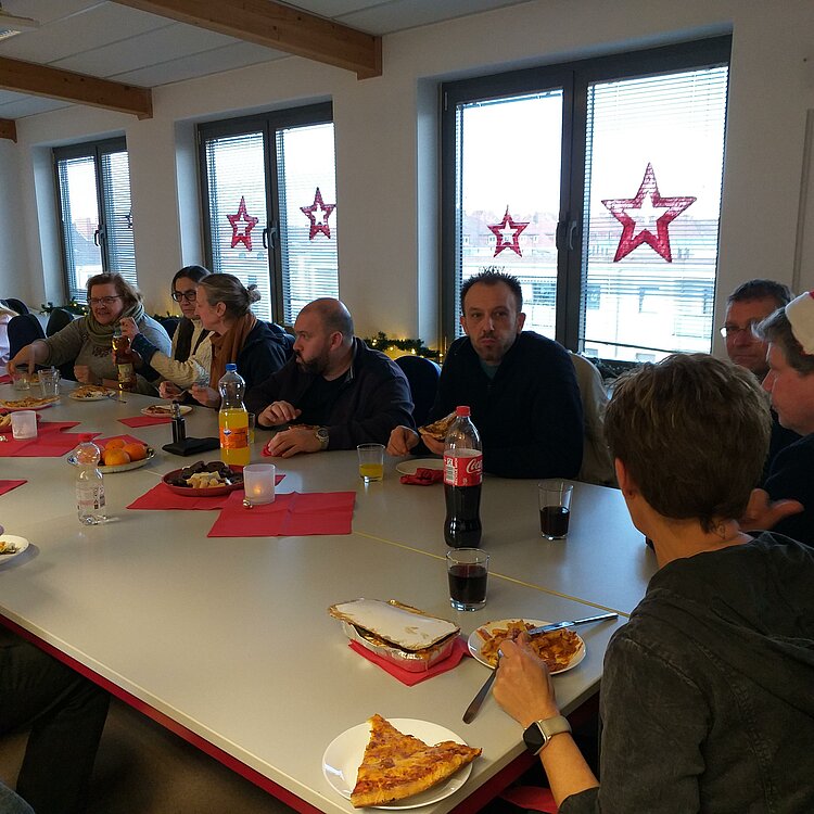 Nikolausfeier Lehrkräfte der Euro-Schulen Hannover sitzen zusammen an einem großen Tisch und essen Pizza und Lasagne.