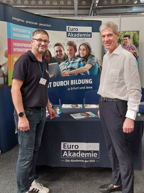 Zwei Mitarbeiter posieren am Euro Akademie Stand für ein Foto.