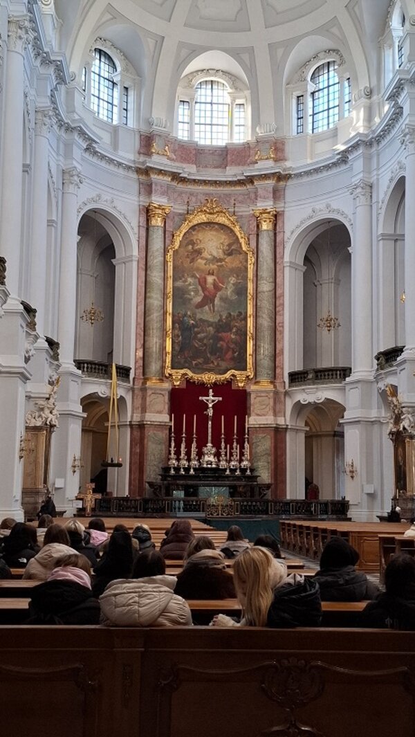 Innenansicht einer barocken Kirche mit Altar, großem Gemälde und sitzenden Besuchern in den Kirchenbänken