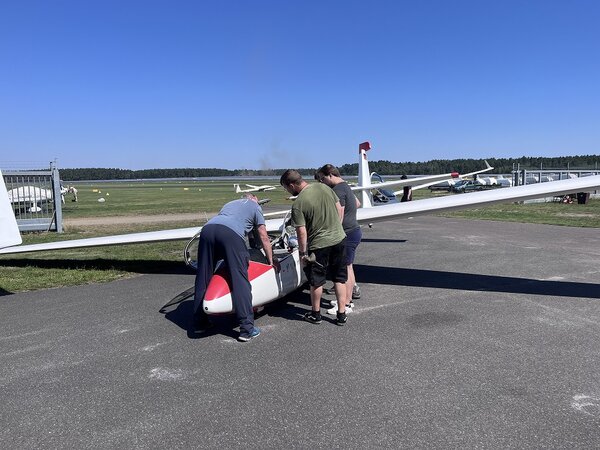 Mehrere Personen stehen an einem Segelflugzeug und schauen gemeinsam in den geöffneten Cockpitbereich.