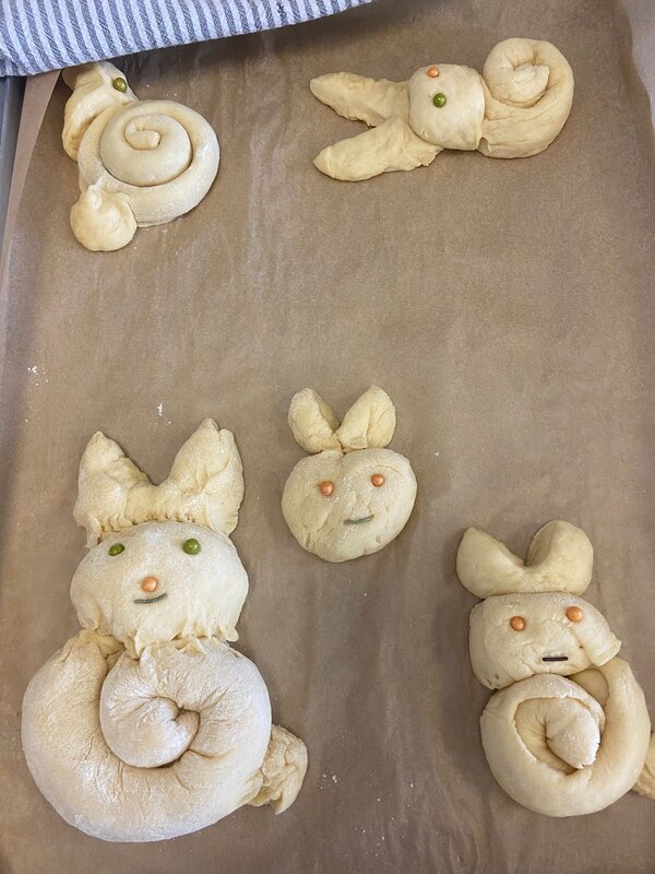 Auf einem Backblech liegen fünf Teiglinge für Osterhasen aus Hefeteig.