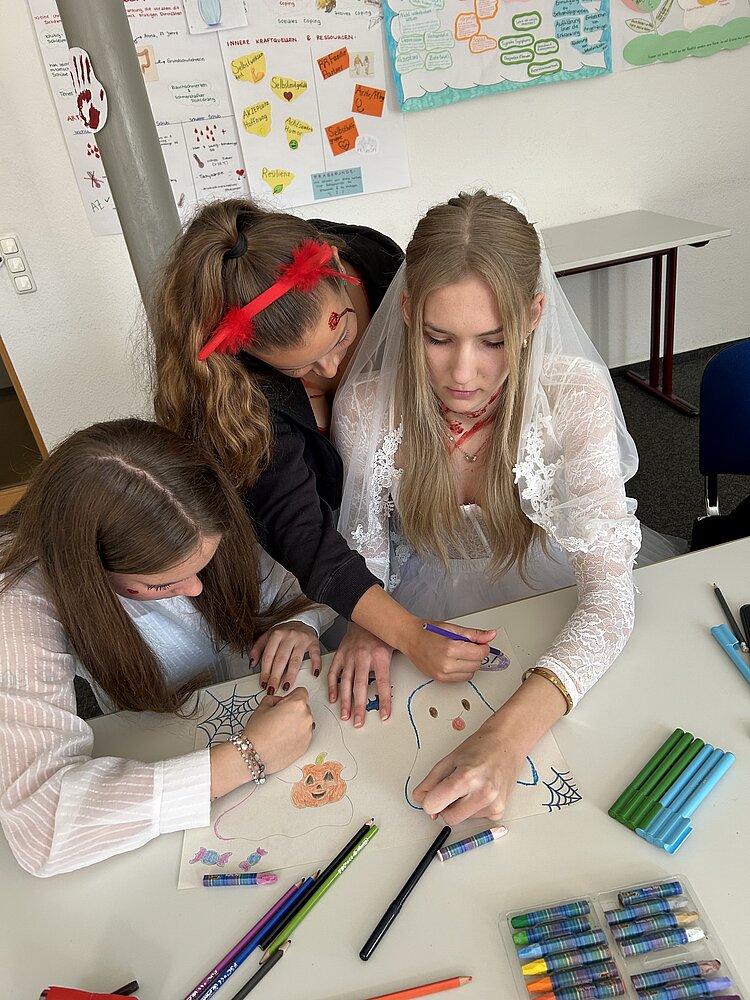 Weitere Nahaufnahme derselben Zeichenszene mit Händen beim Ausmalen eines Geistes und Kürbisses.